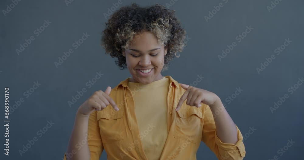 Slow motion portrait of joyful African American woman pointing down recommending content asking to follow on grey background. People and body language concept. Slow motion portrait of joyful African American woman pointing down recommending content asking to follow on grey background. People and body language concept.