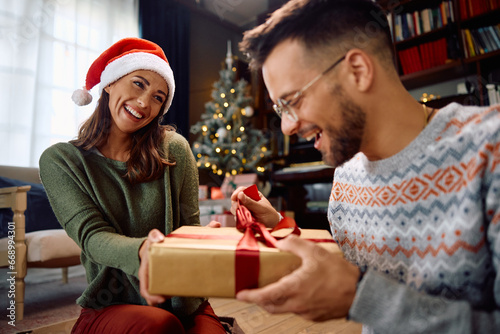 Happy woman surprising her boyfriend with Christmas present at home.