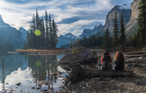 Two young friends sitting on a log having a good relationship, sitting and talking, looking at the view of Spirit Island. Beautiful Spirit Island in Maligne Lake, Jasper National Park, Alberta, Canada