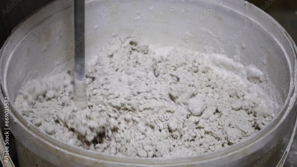 Builder Mixes Solution in Bucket. Plaster. Construction Site. Rotating Nozzle. Cement. Putty. Construction Mixture Diluted with Water. Renovation Work in Premises. Kneading. Close up, slow motion. Builder Mixes Solution in Bucket. Plaster. Construction Site. Rotating Nozzle. Cement. Putty. Construction Mixture Diluted with Water. Renovation Work in Premises. Kneading. Close up, slow motion.