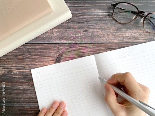 デスクでノートに字を書く女性の手元 photo