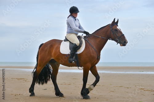 Young female horse rider and her large bay horse enjoy a ride on the beach in Wales UK.The horse looks alert and beautiful with her ears forward as she enjoys the empty space and sandy floor.