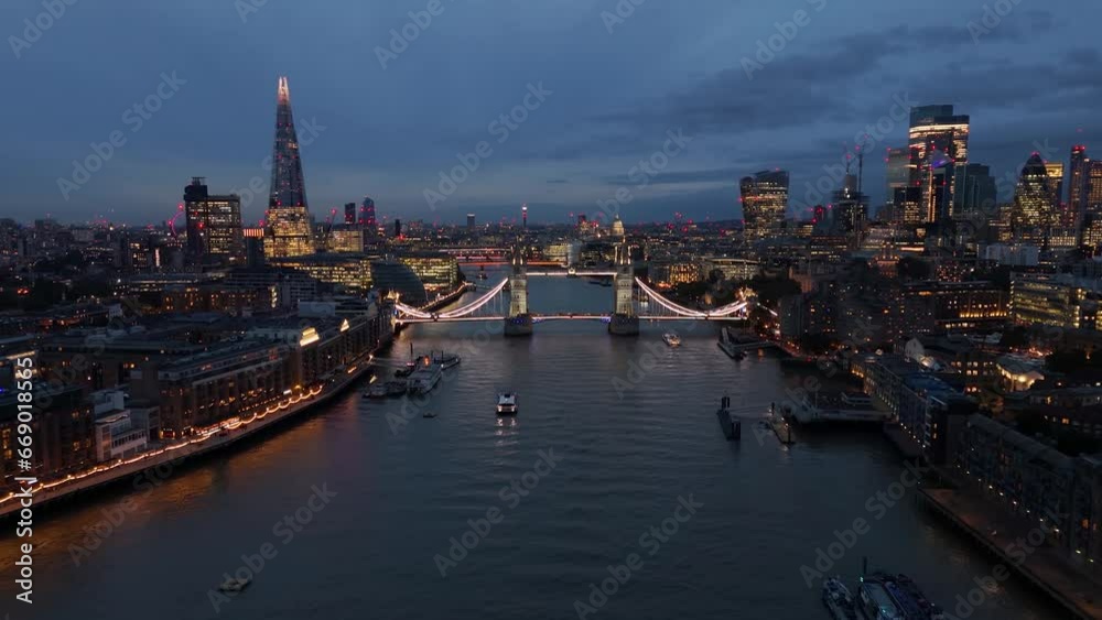 Aerial panoramic to closeup view of the illuminated Tower Bridge and London skyline by night, United Kingdom