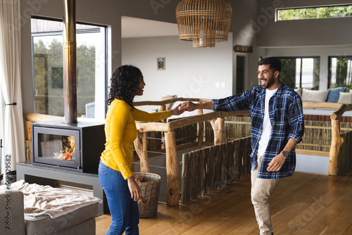 Happy biracial couple dancing and smiling in living room at home photo