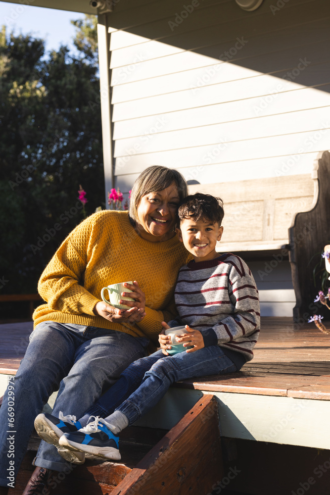 Portrait of happy biracial grandmother and grandson drinking tea sitting in garden Portrait of happy biracial grandmother and grandson drinking tea sitting in garden