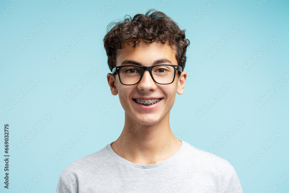 Portrait of smiling smart school boy with braces wearing glasses isolated on blue background. Education concept - obrazy, fototapety, plakaty 
