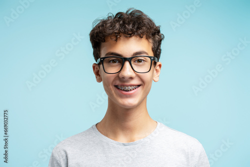 Portrait of smiling smart school boy with braces wearing glasses isolated on blue background. Education concept