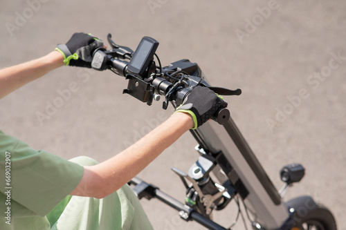 A woman controls a wheelchair using a special manual device. Close-up of female hands on electric handbike. 