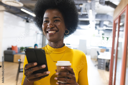 Happy african american casual businesswoman using smartphone over colleagues working in office photo