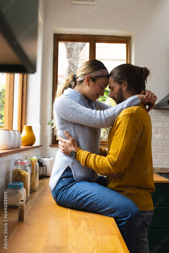 Happy, romantic caucasian couple embracing sitting on worktop and standing in kitchen, copy space Happy, romantic caucasian couple embracing sitting on worktop and standing in kitchen, copy space