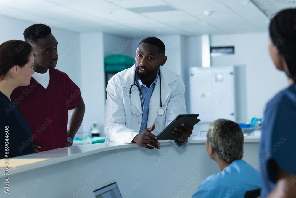 Diverse male and female doctors discussing work, using tablet at reception desk at hospital Diverse male and female doctors discussing work, using tablet at reception desk at hospital