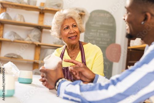 Two happy diverse female and male potters discussing about job in pottery studio
