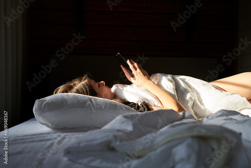 Woman in bed checking social media with smartphone