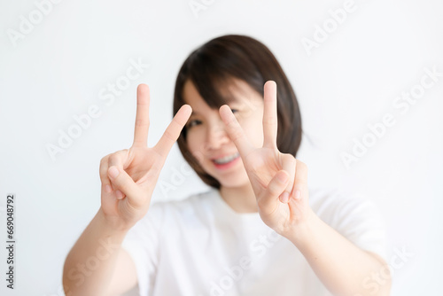 Asian woman holds up two fingers and smiles on white background.