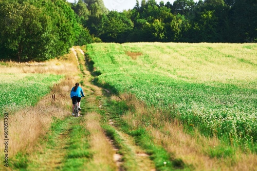 back view of a young woman riding a bicycle in the countryside. traveling by bike. outdoor activity.