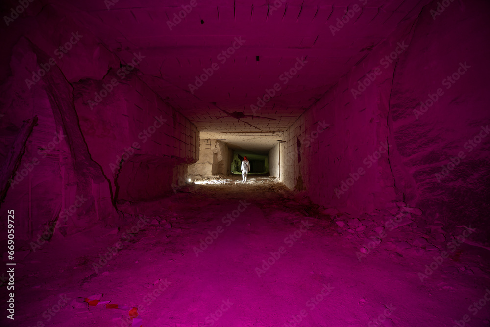 A woman stands in long tunnels deep underground. Stone mining tunnels and caves, Red lights