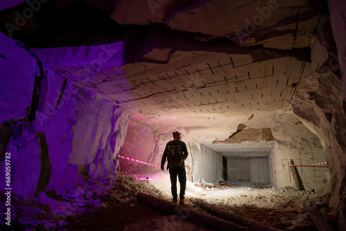A man with powerful flashlights explores dangerous tunnels, old abandoned quarry mines near the city of Sataniv, Ukraine. Cracks and chasms. Back view photo