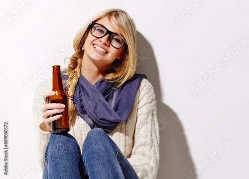 Happy woman, portrait and relax with beer of nerd, geek or hipster against a studio background. Attractive female person or model smile with glasses, nerdy or fashion style holding bottle of alcohol photo