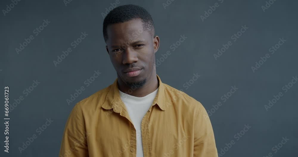 Slow motion portrait of unhappy African American man sighing shaking head and crossing arms on grey background. People and negative emotion concept. Slow motion portrait of unhappy African American man sighing shaking head and crossing arms on grey background. People and negative emotion concept.