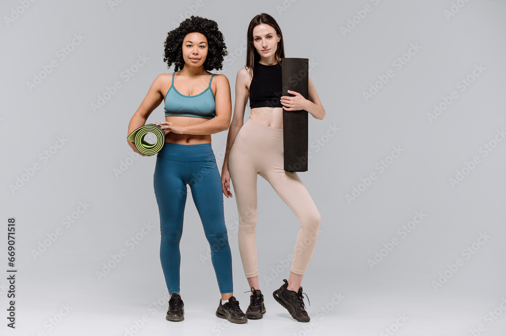 Fototapeta premium Two women in sportswear wiht yoga mat standing on gray copy space background