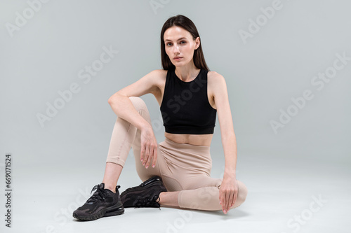 Young model in sportswear sitting on studio floor, posing for outfit advertising