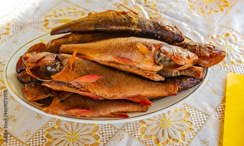 Hot smoked river perch fish on a ceramic plate close-up on a plastic tablecloth