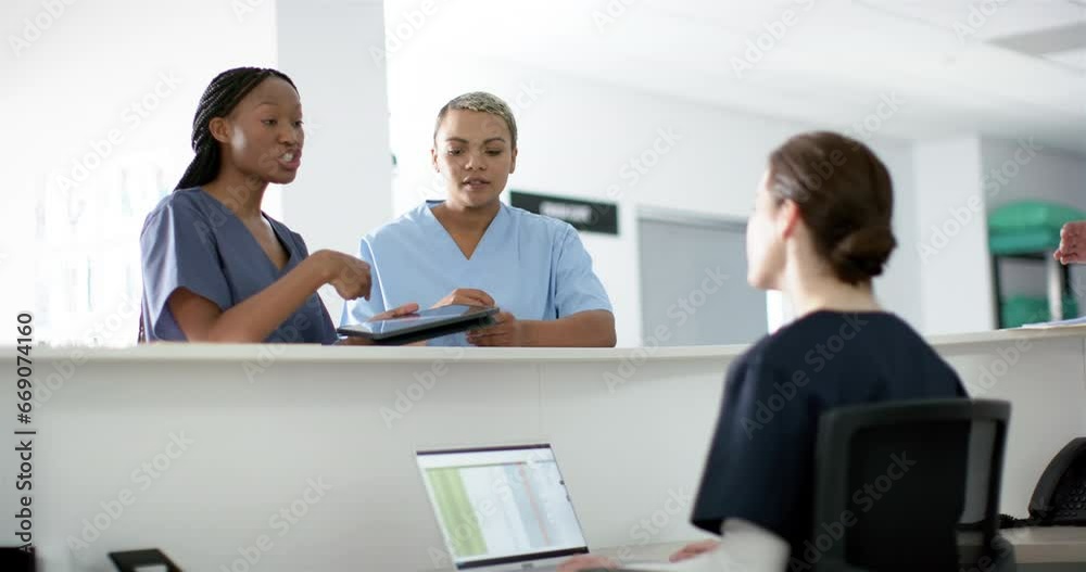 Diverse female doctors discussing work, using tablet at reception desk at hospital, slow motion Diverse female doctors discussing work, using tablet at reception desk at hospital, slow motion
