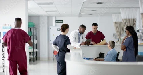 Diverse doctors discussing work, using tablet at reception desk at hospital, slow motion photo