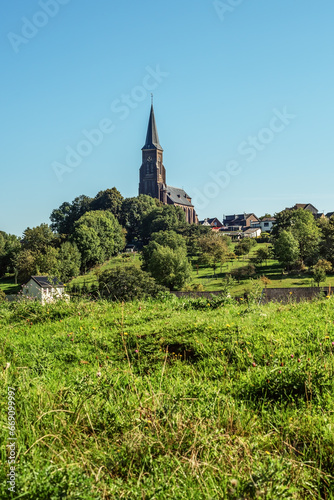 Village with church in lush hilly countryside with blue sky.
