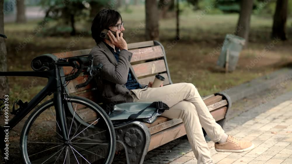 Businessman in suit sits on bench, his phone in hand, his eyes focused on screen Businessman in suit sits on bench, his phone in hand, his eyes focused on screen