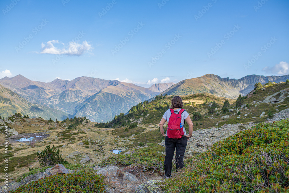 young curvy caucasian girl standing resting on the mountain while she is trekking with her hands on her waist and enjoying the landscape