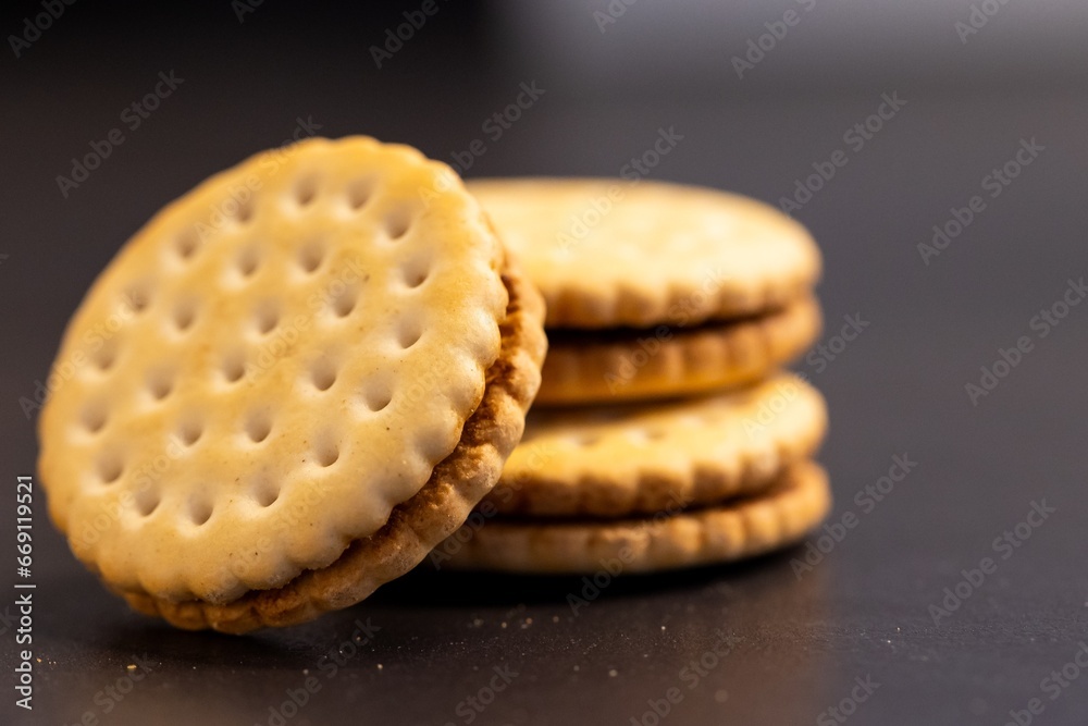 A closeup portrait of tasty round cookies stacked on top of each other with one fallen off on a kitchen counter. The delicious snack has a biscuit on each side and is filled with chocolate cream.