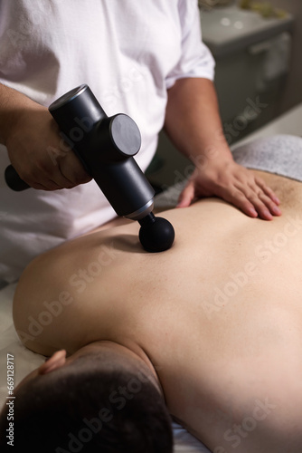 Massage gun treatment. Physical therapist treating injury of back man muscle of gun percussion massager. Doctor doing massage of back guy in clinic room. Medical therapy concept. Copy ad text space