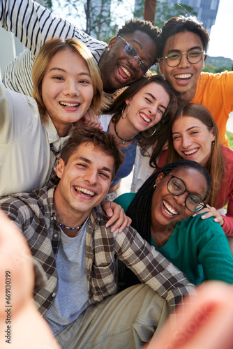 Fotografie Happy group of multiethnic classmate taking a selfie together outdoors in the university campus, looking at camera cheerfully raising arms, celebrating last day