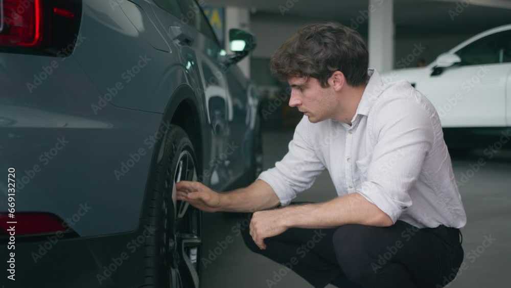 Caucasian man buyer client shopper in automobile salon male businessman choose new auto transport rental service touch wheels of car check quality of tires thinking purchase shopping decision repair