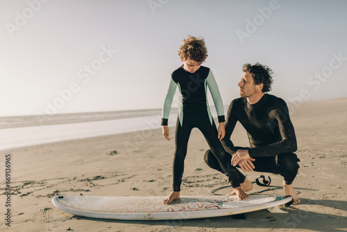 Father guiding his son on proper surfing stance at the beach photo