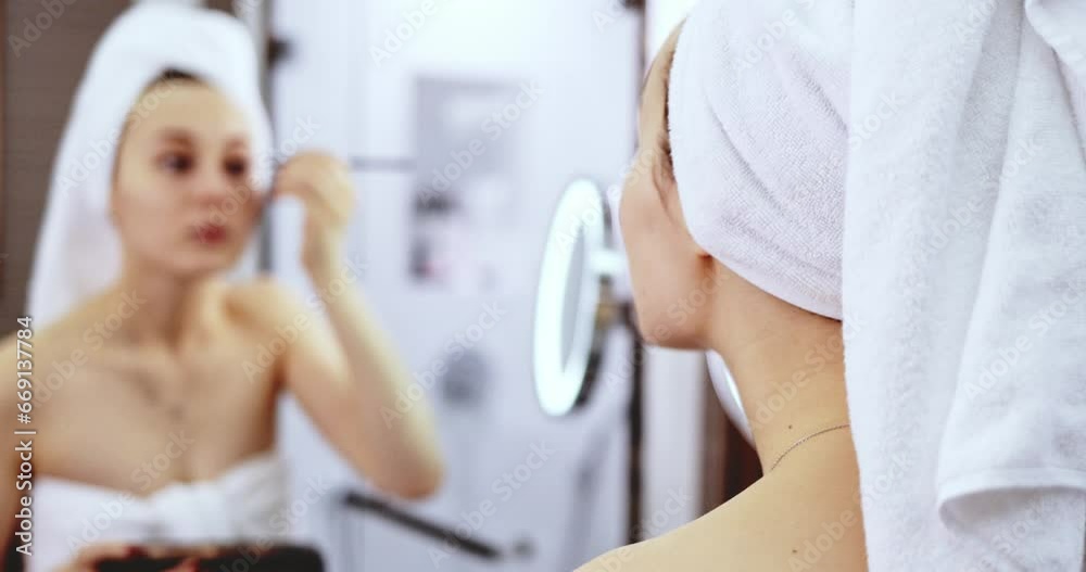 Young Woman Applying Make Up. SLOW MOTION. Girl apply nude eye shadow with brush, standing before the mirror in the bathroom after shower. Everyday beauty rituals.