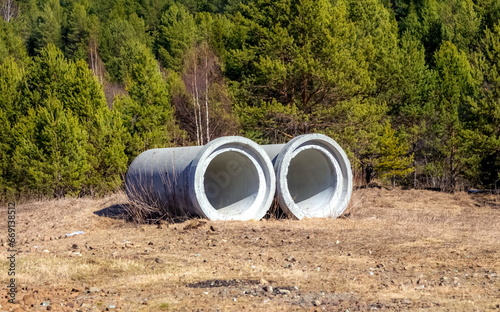 Large diameter concrete pipes in close-up against the background of trees in spring