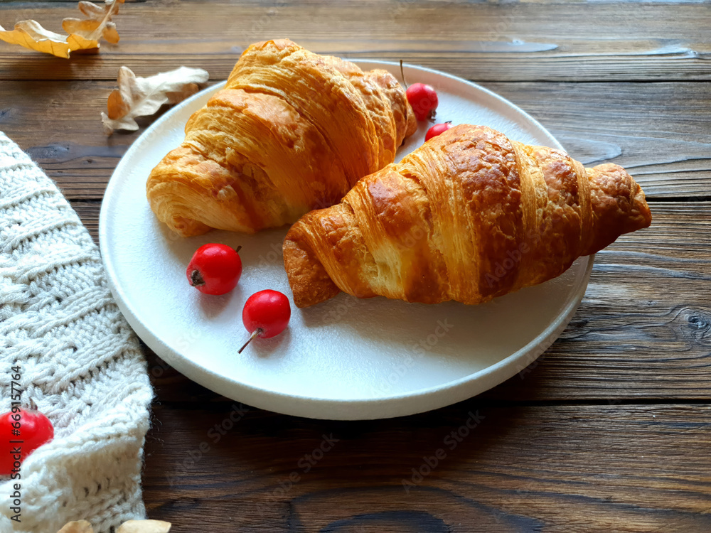 There is a plate with freshly baked croissants on the wooden table. Close-up.