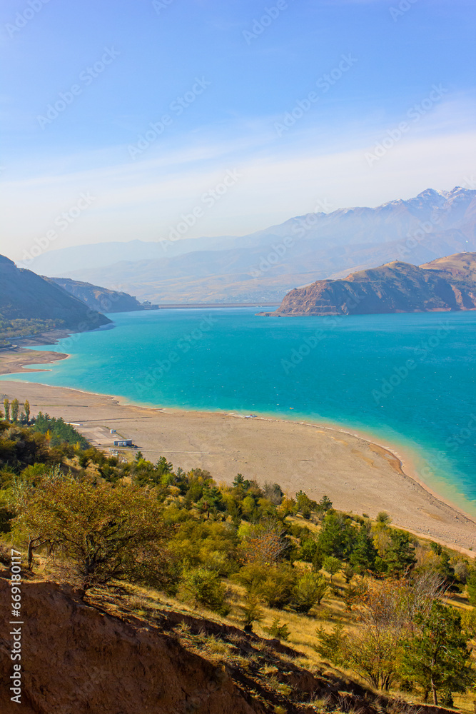 Fototapeta premium View of the Charvak reservoir from the shore. Autumn landscape of Uzbekistan: a bright blue lake and yellowed grass.