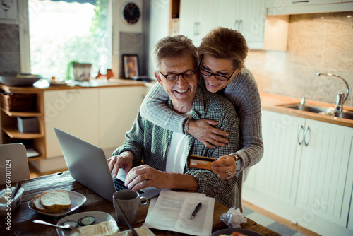 A joyful senior couple shares a moment while making an online purchase at home photo