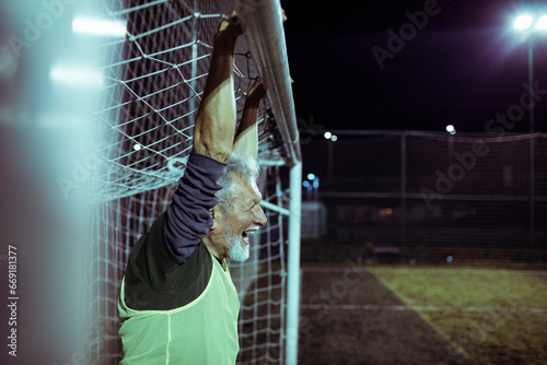 Elderly goalkeeper guarding the goal on a soccer pitch at night photo