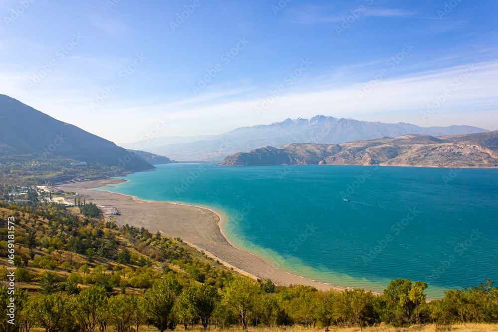 View of the Charvak reservoir from the shore. Autumn landscape of Uzbekistan: a bright blue lake and yellowed grass.