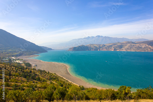 View of the Charvak reservoir from the shore. Autumn landscape of Uzbekistan: a bright blue lake and yellowed grass.