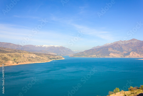 View of the Charvak reservoir from the shore. Autumn landscape of Uzbekistan: a bright blue lake and yellowed grass.