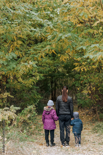A family, a mother with her son and daughter, are walking through the forest in an outdoor park, holding hands. Photography, portrait, lifestyle.