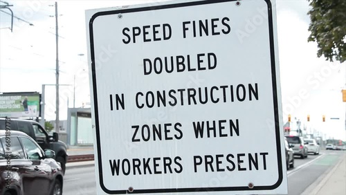 speed fines doubled in construction zones when workers present square exterior white black sign writing caption text with cars vehicles traffic passing driving moving behind photo