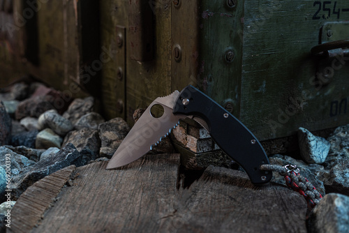 Knife with serrated blade. Knife on a stump and stones. Pocket knife with lanyard. Front view. photo