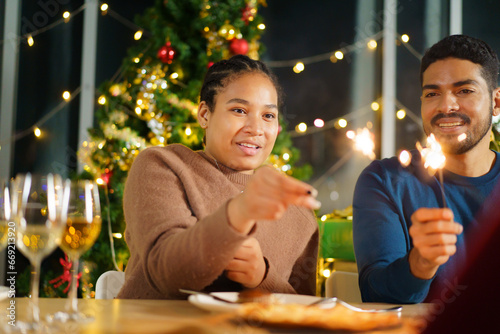 Group of diverse ethnicity young people enjoy celebrating a Christmas and New Year party together with a lot of foods and drinks and enjoy playing with sparkling bengal light - fireworks together.