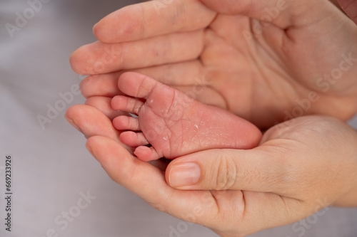 A young mother holds the foot of her newborn son. Close-up of female hands. 